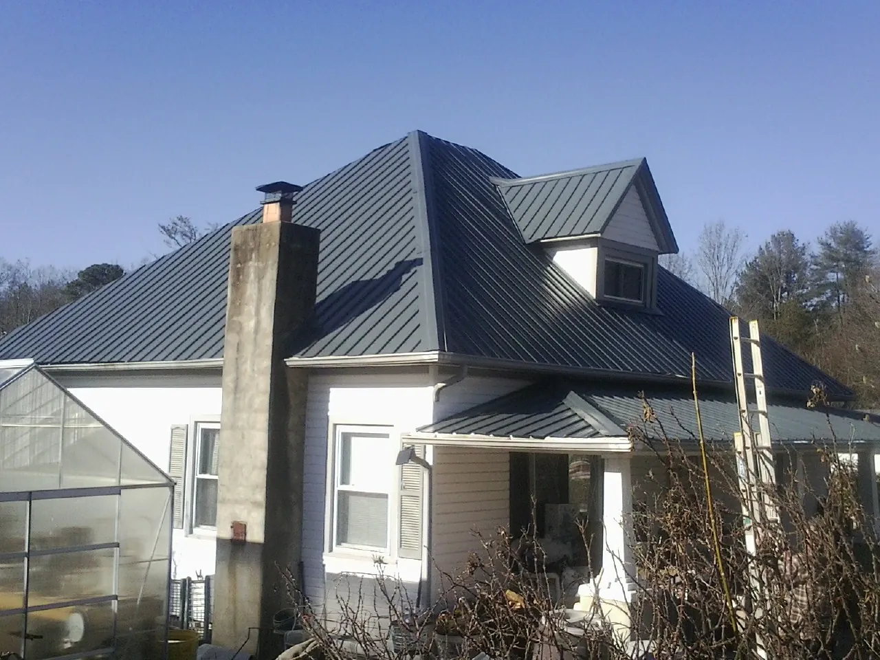 Dark blue standing seam metal roof on a white farmhouse with dormer — Slate & Tile Roof Repair by Roofing Brothers in Fort Ripley