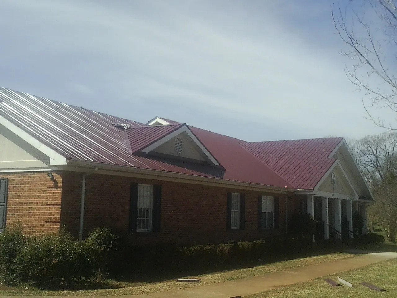 Red metal roof with gabled entries on a long brick building, from a Hail Damage Roof Repair job in Fort Ripley