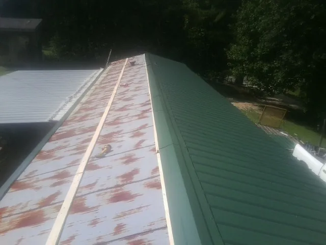 Old rusted panels beside newly installed green metal roofing — Wind Damage Roof Repair by Roofing Brothers in Fort Ripley