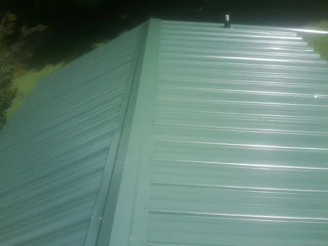 New green metal panels meeting at the ridge of a roof — Flat Roof Repair work by our crew in Fort Ripley