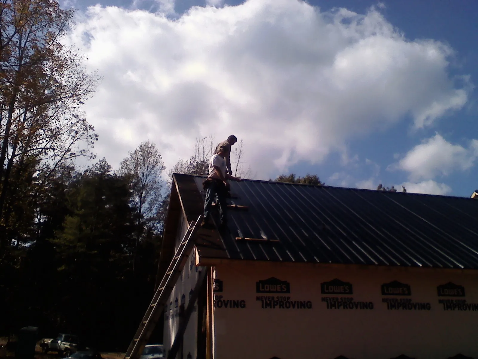 Roofer fastening dark metal panels high against a cloudy sky, from a Roof Inspection job in Fort Ripley
