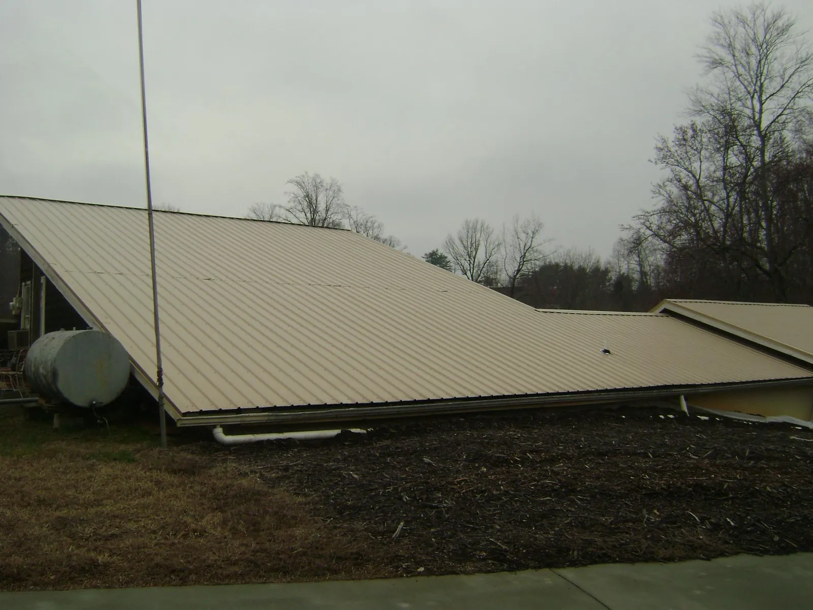 Wide tan metal roof plane seen from the ground beside a propane tank in Fort Ripley