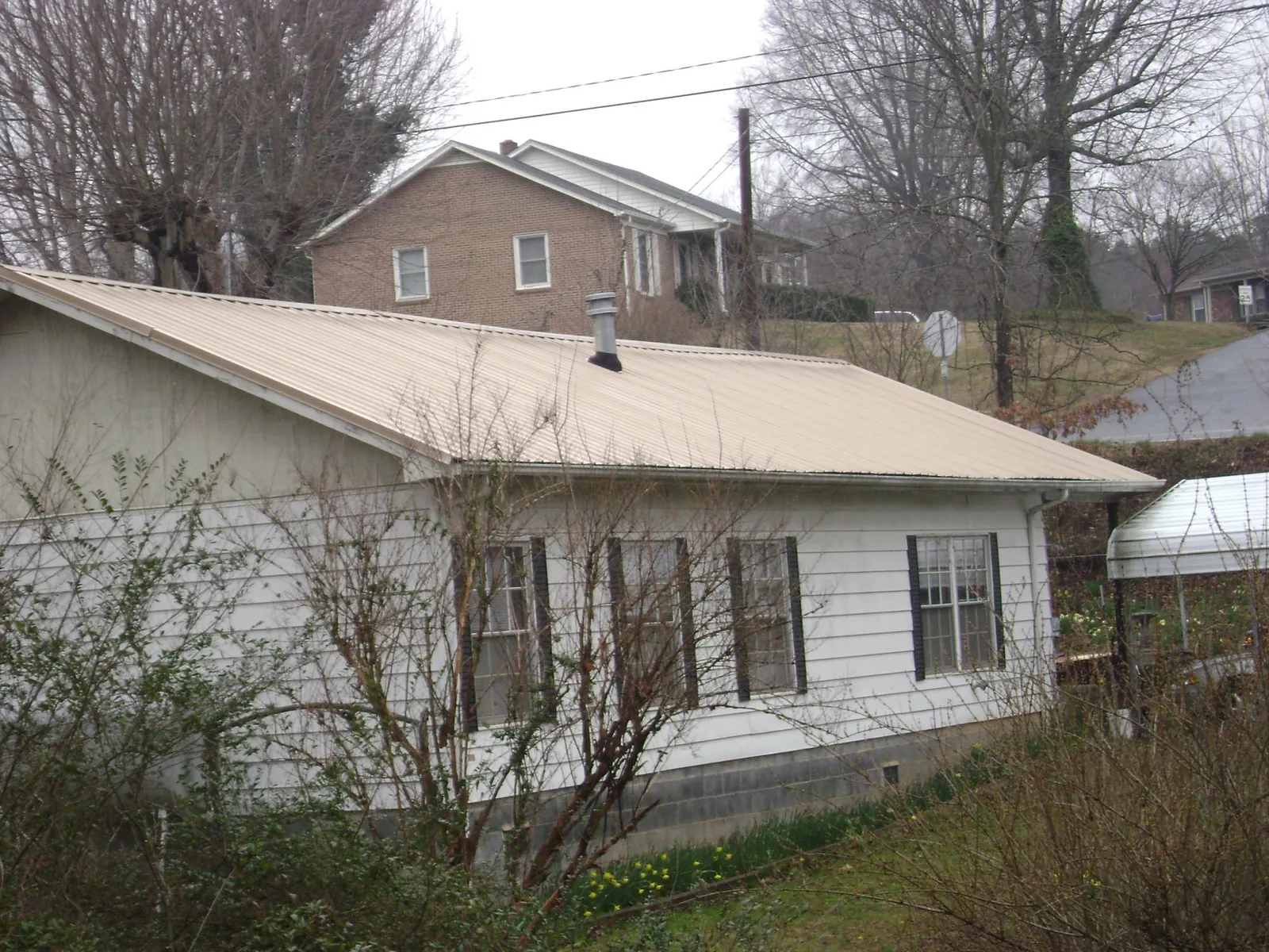 Tan metal roof on a white sided house set into a hillside — Commercial Roofing by Roofing Brothers in Fort Ripley