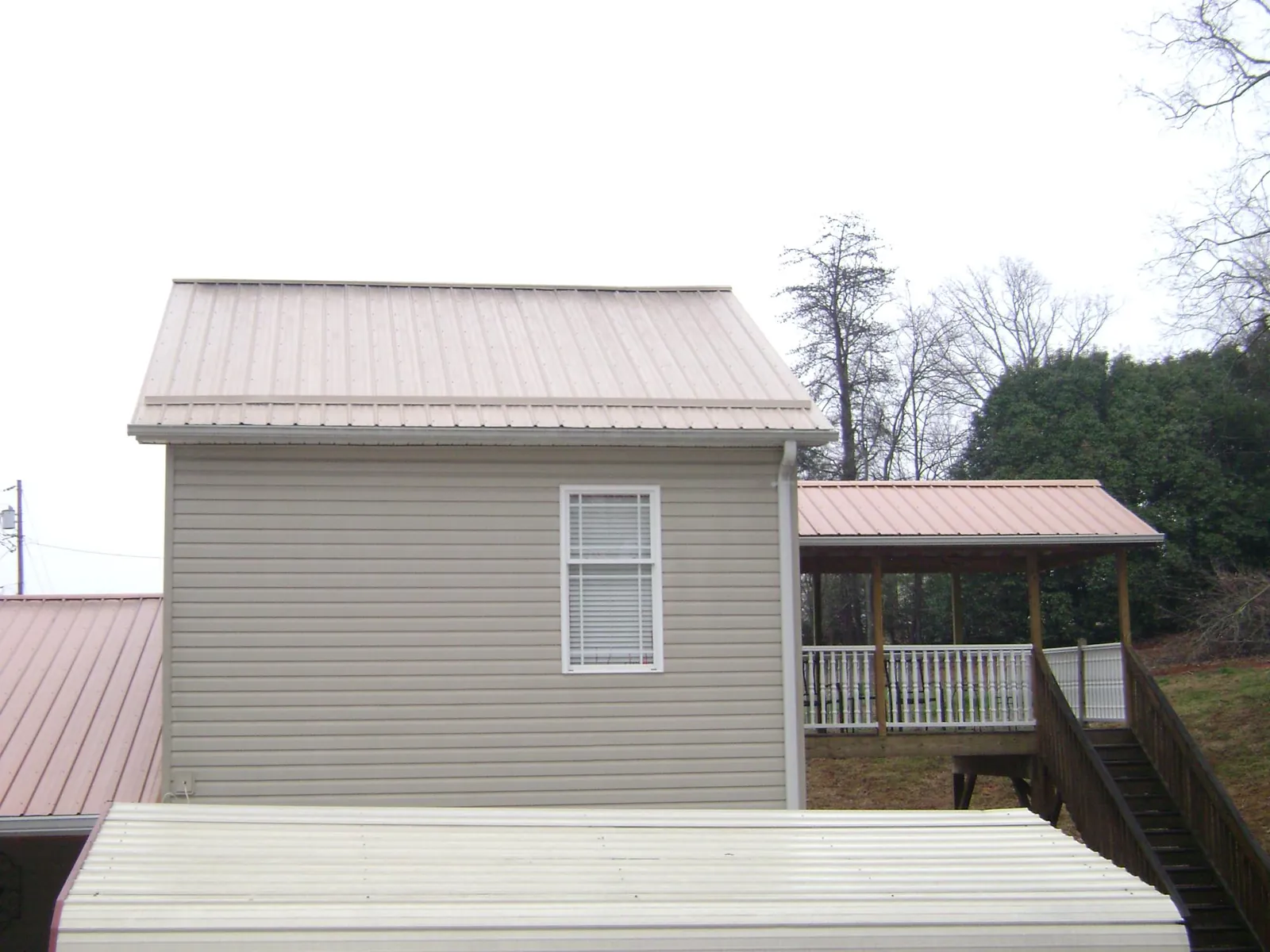 Tan metal roofs on a two story addition and attached porch, from a Roof Replacement job in Fort Ripley